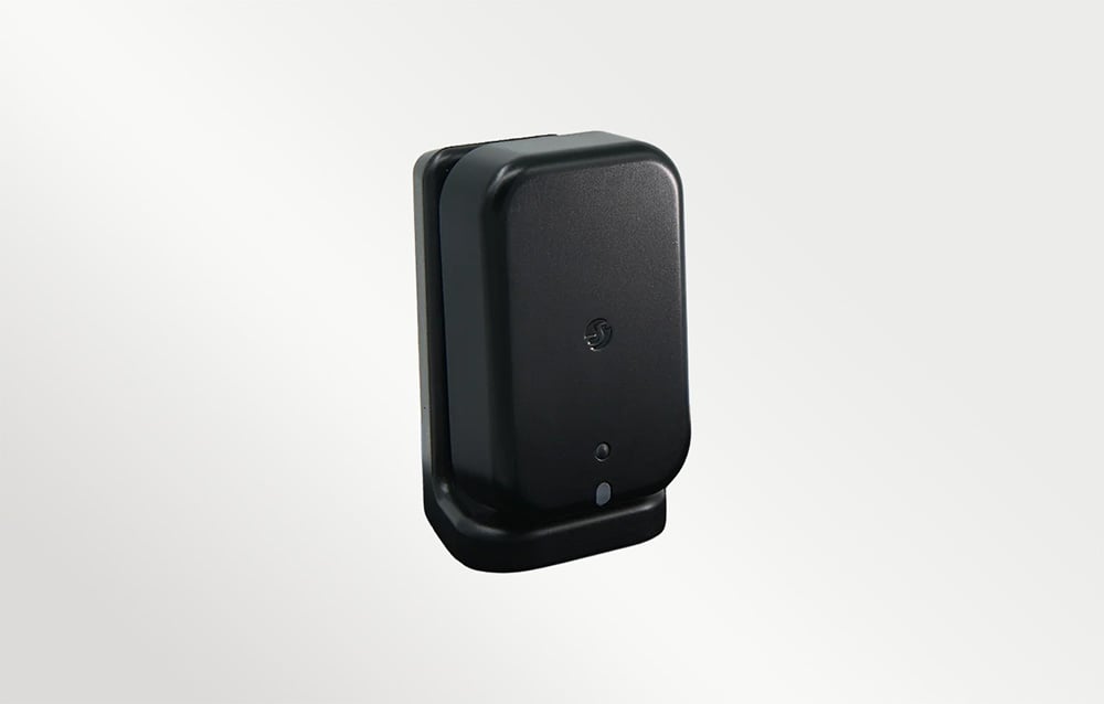 Wall-mounted presence sensor in a black plastic housing, photographed against a light background.