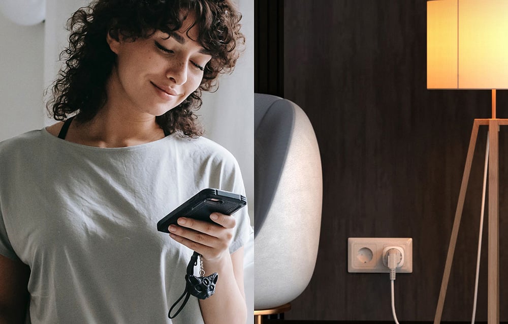 A smiling woman holding a smartphone; a lamp is lit on the right side of the room