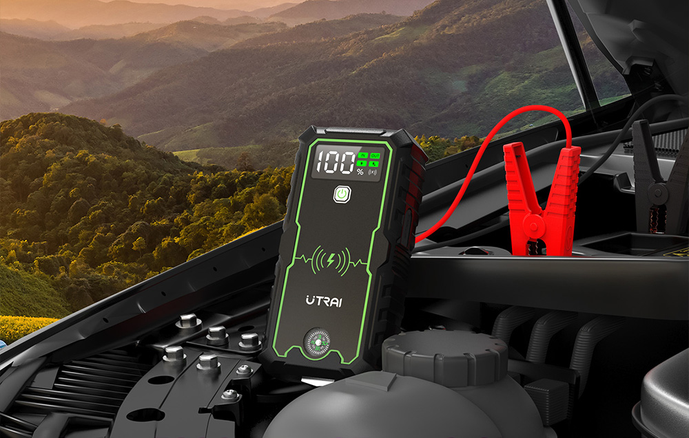A black battery charger with a red clamp connected under the hood of a car.