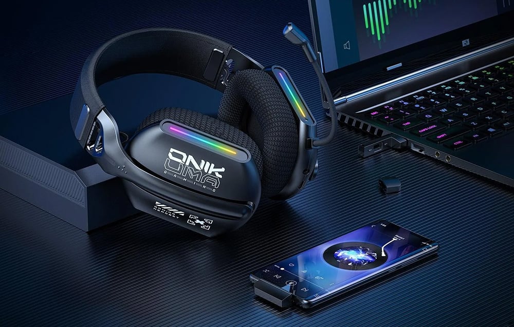 Onikuma headphones lying on a table next to a smartphone and laptop