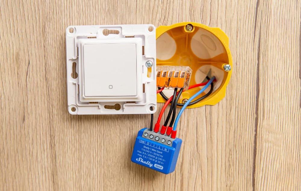 A blue controller connected by colored wires to a wall switch.