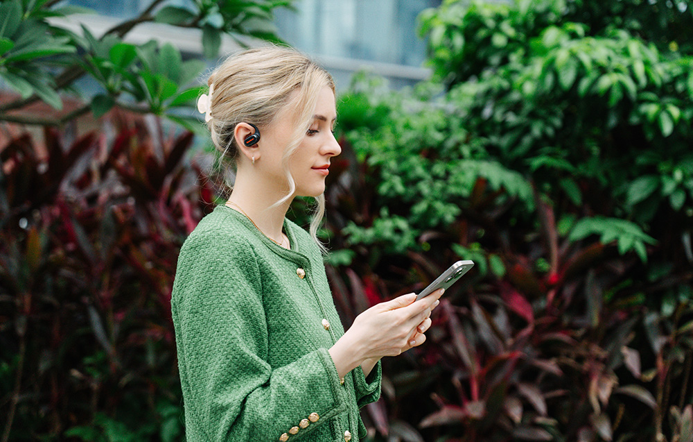 Woman outside holding phone and wearing black wireless in-ear headphones without microphone
