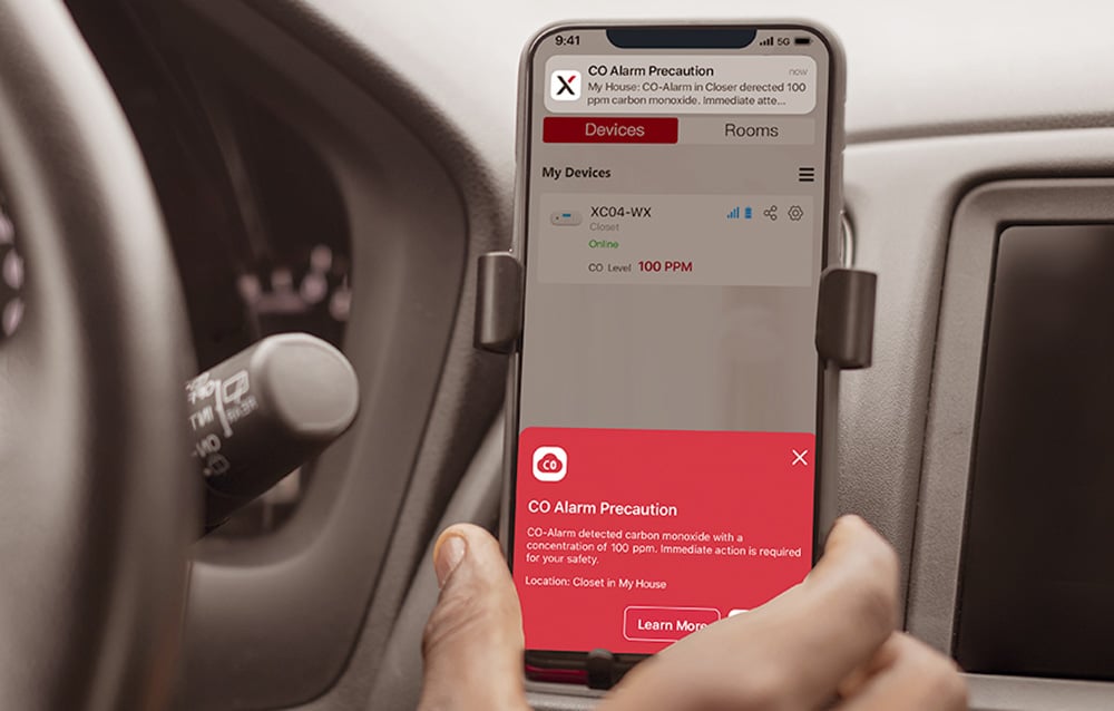 Telefon w samochodzie pokazujący czerwony alert CO z poziomem 100 PPM