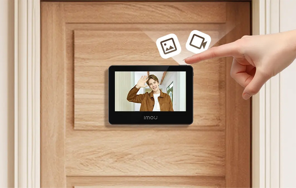 An index finger pointing at a button on the door viewer screen showing a smiling man; photo and video icons