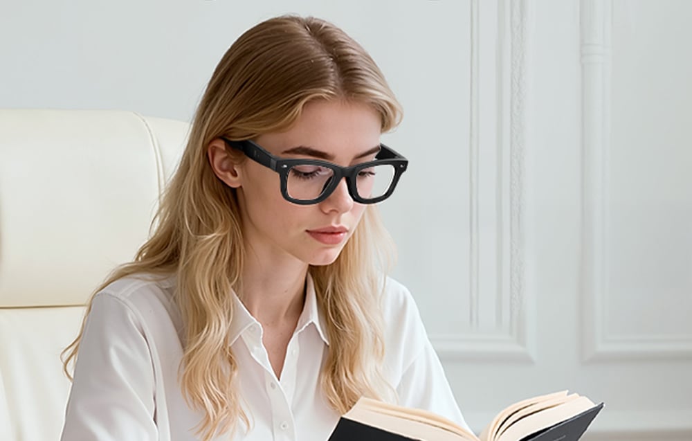 A woman with blonde hair and sunglasses sits in an armchair reading a book