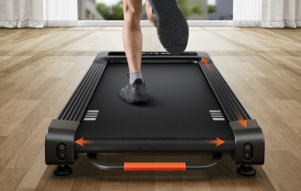 Legs of a person exercising on a black treadmill with orange arrows on the housing, rear view