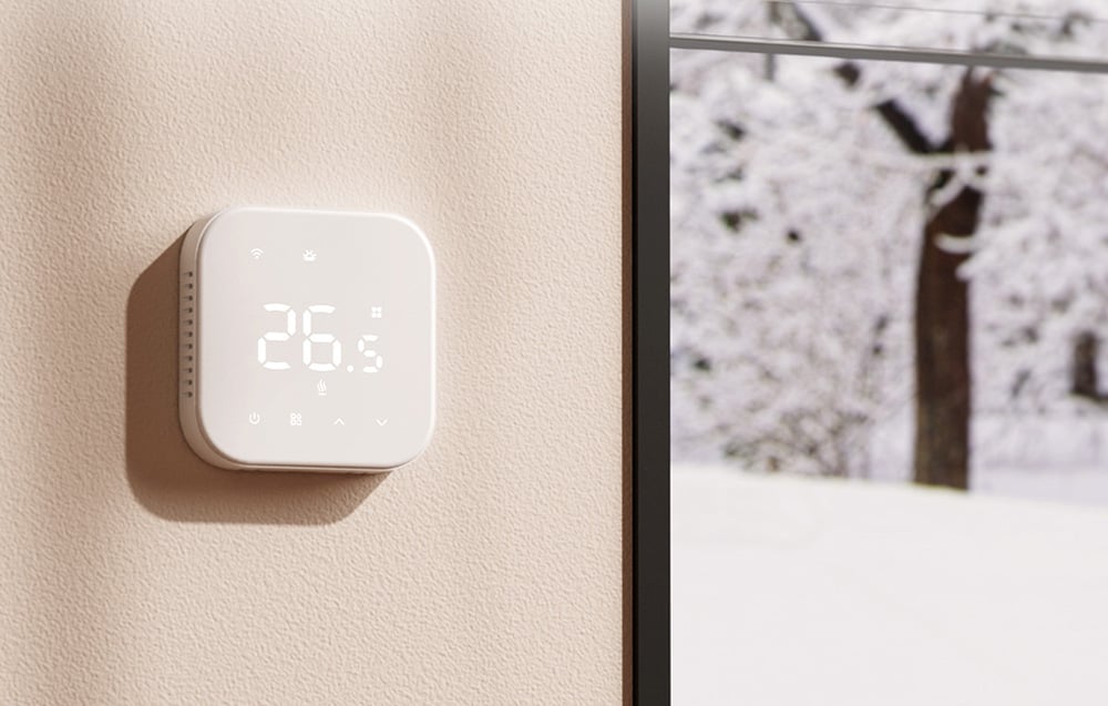 White digital thermostat on the wall next to a window with a winter landscape