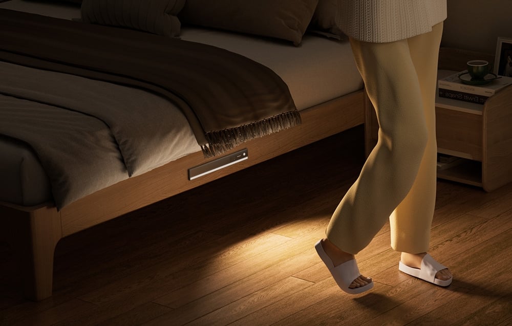 Yeelight closet light mounted under the bed illuminating the floor next to the standing person.