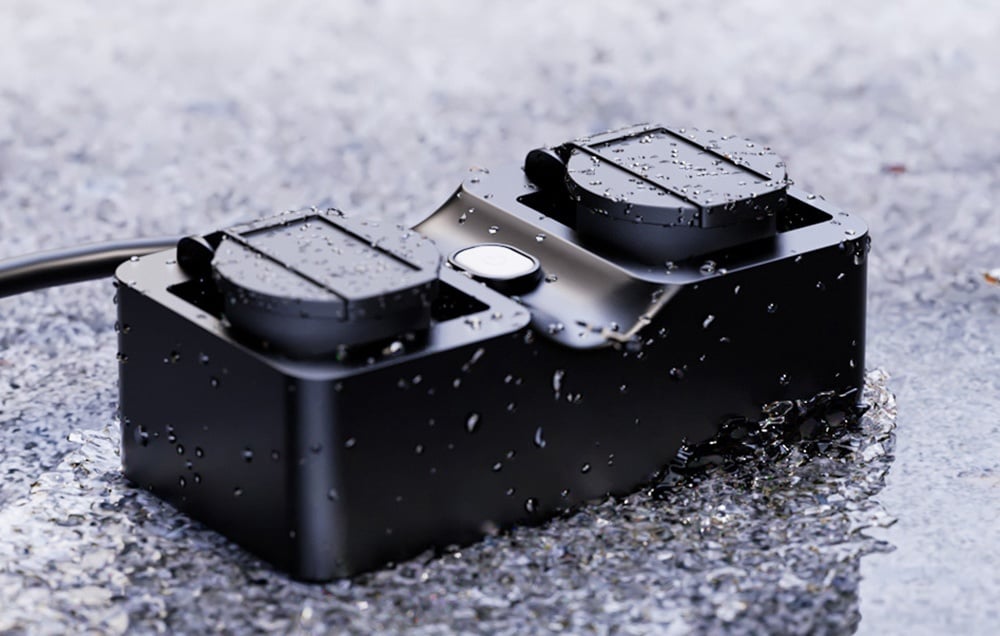 Black waterproof power strip with two outlets, lying on wet pavement with water drops