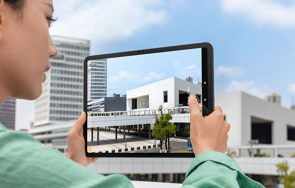 A person photographing architecture through a tablet, visible camera interface on the device's screen