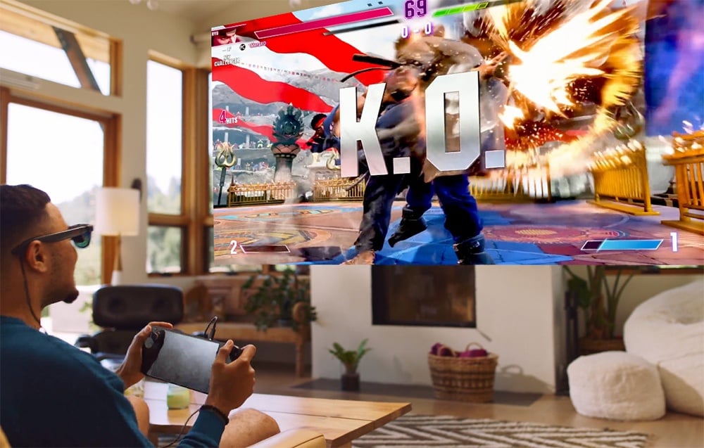 A man wearing XR glasses plays a fighting game on a portable console visible on a large screen