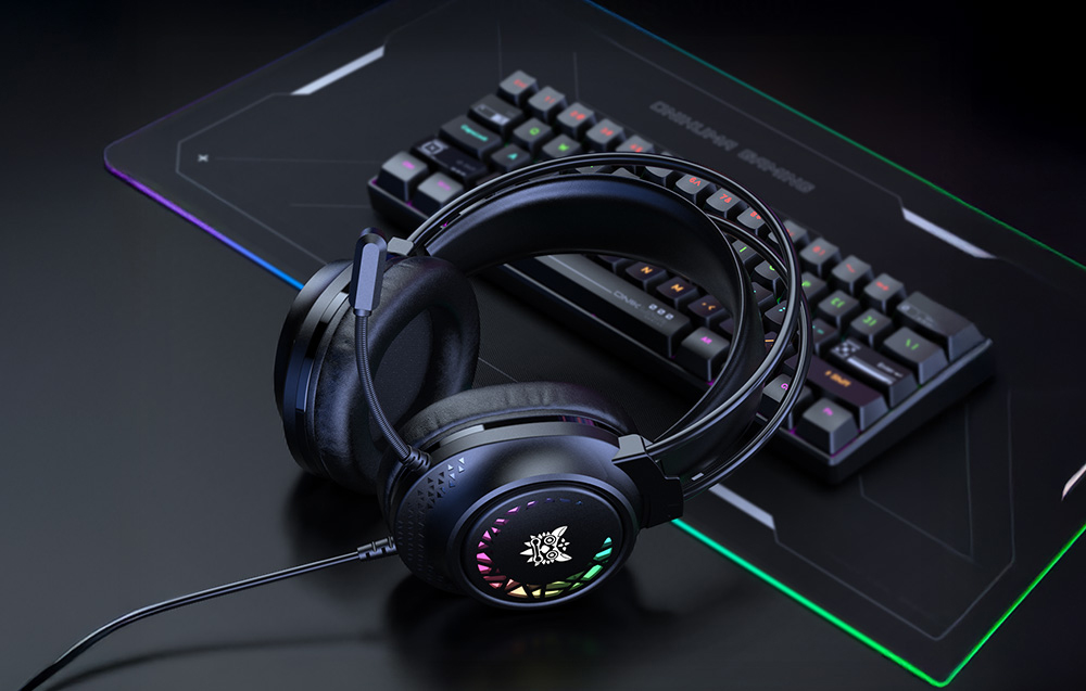 Black gaming headphones with colored backlighting leaning against a keyboard on a dark desk
