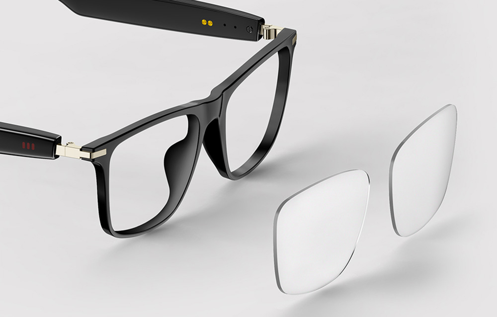 Glasses with thick black frames and two separate lenses lying next to them on a light background.