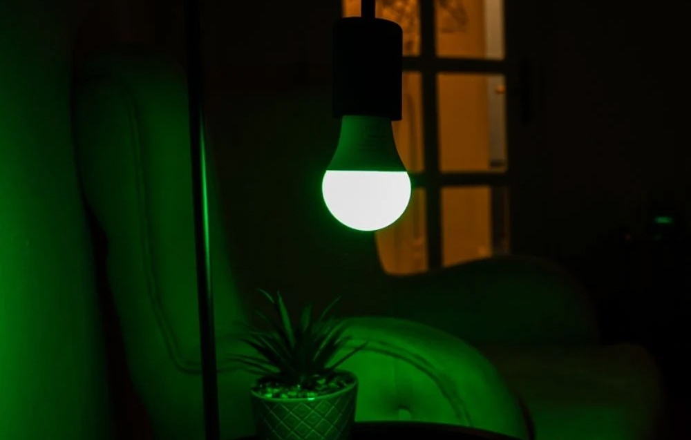 A green-glowing light bulb hanging in a dark room above a small potted plant