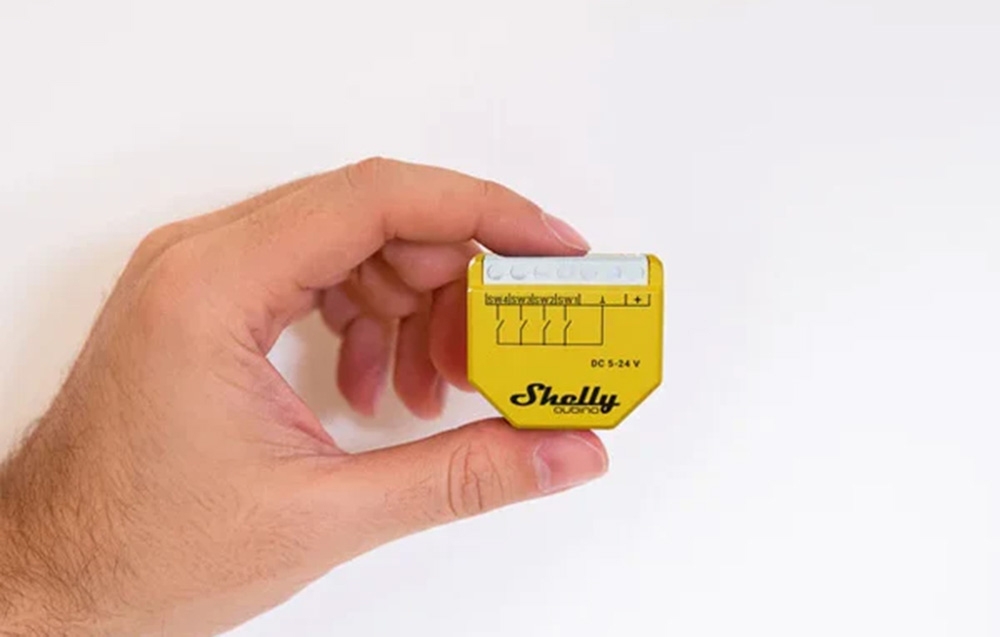 A person holding a yellow Shelly switch between their fingers against a white background