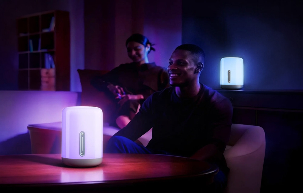 Two people in a living room illuminated by colorful, purple-blue light from two lamps
