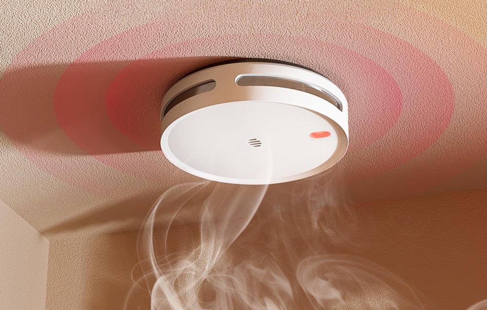Smart smoke detector on a light-colored ceiling, with white smoke rising below