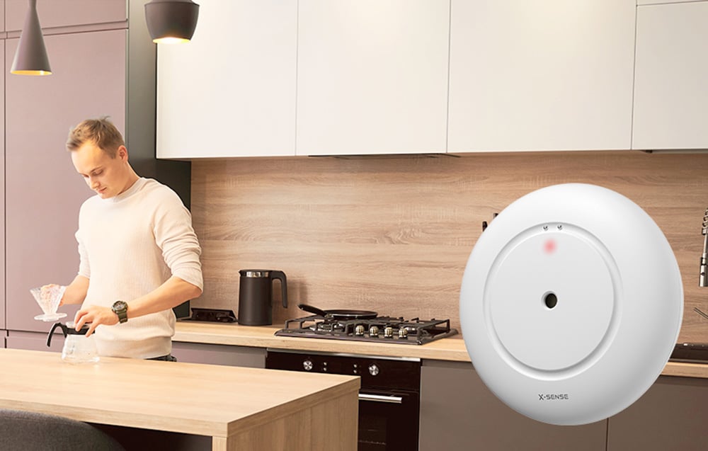 A man making coffee in the kitchen, next to a close-up view of the round, white X-Sense flood sensor