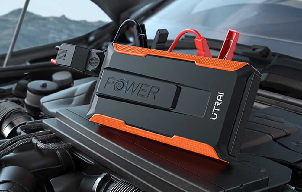A portable car jump starter with battery clamps attached, located in the engine compartment.