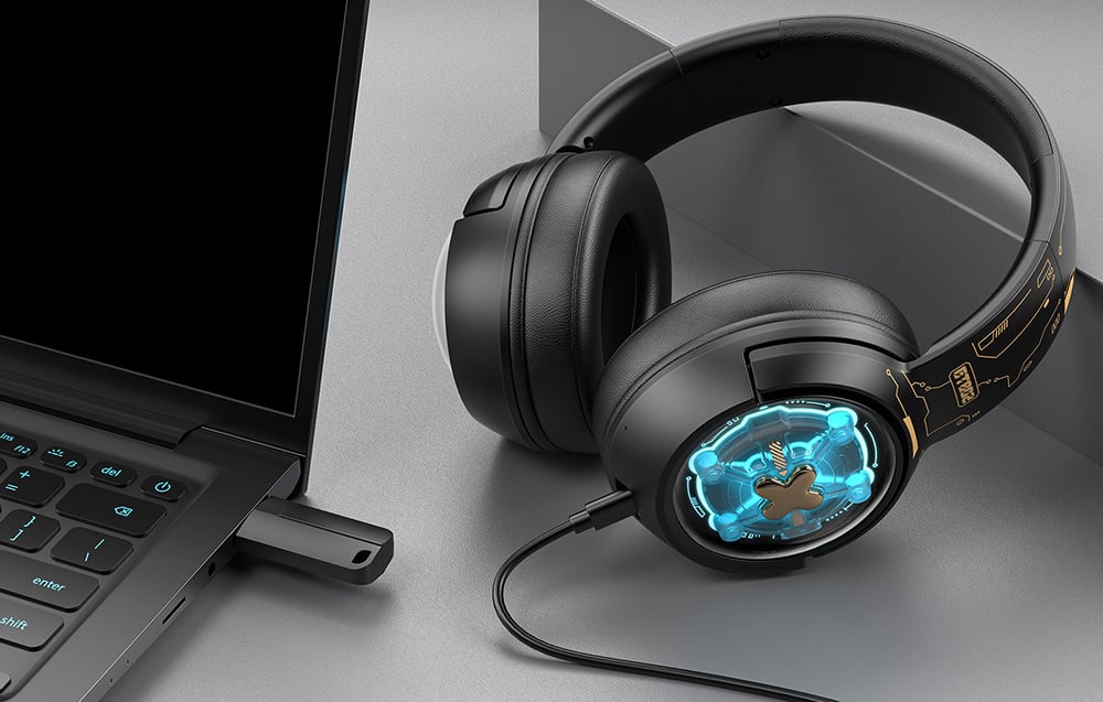 Onikuma gaming headphones lying on a desk next to a laptop with a USB adapter connected