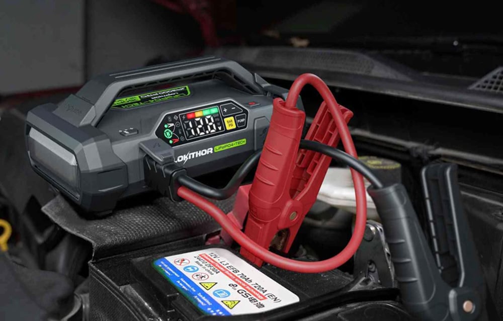 A portable device with clamps connected to the battery under the hood of a car.