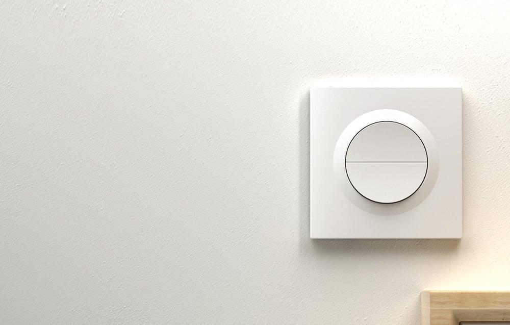 White wall switch with a round button divided into two zones, mounted on a bright wall