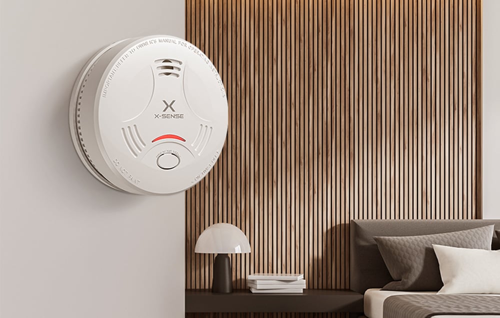 Detektor dymu X-Sense z czerwoną diodą na ścianie w nowoczesnym salonie z drewnianymi lamelami