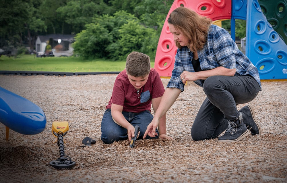 A woman and a boy use a metal detector in a playground