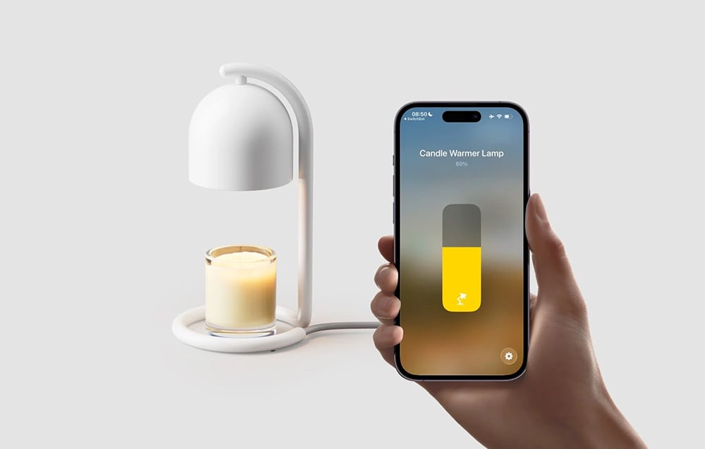 A hand holding a smartphone with the SwitchBot app showing a slider set to 60%, with a white candle warmer and a scented candle in a glass container in the back