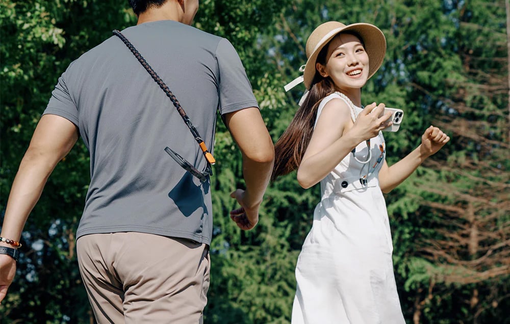 A man walking behind a woman in a white dress and hat, both wearing PGYETCH belts
