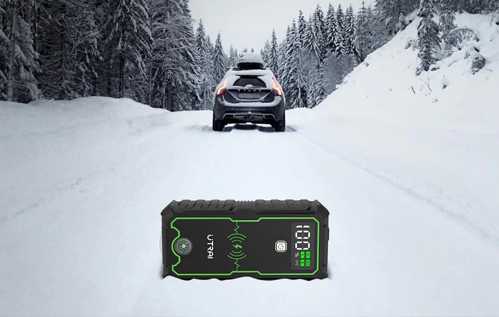 A jump starter lying on a snow-covered road, with a car standing in the background against a winter backdrop.