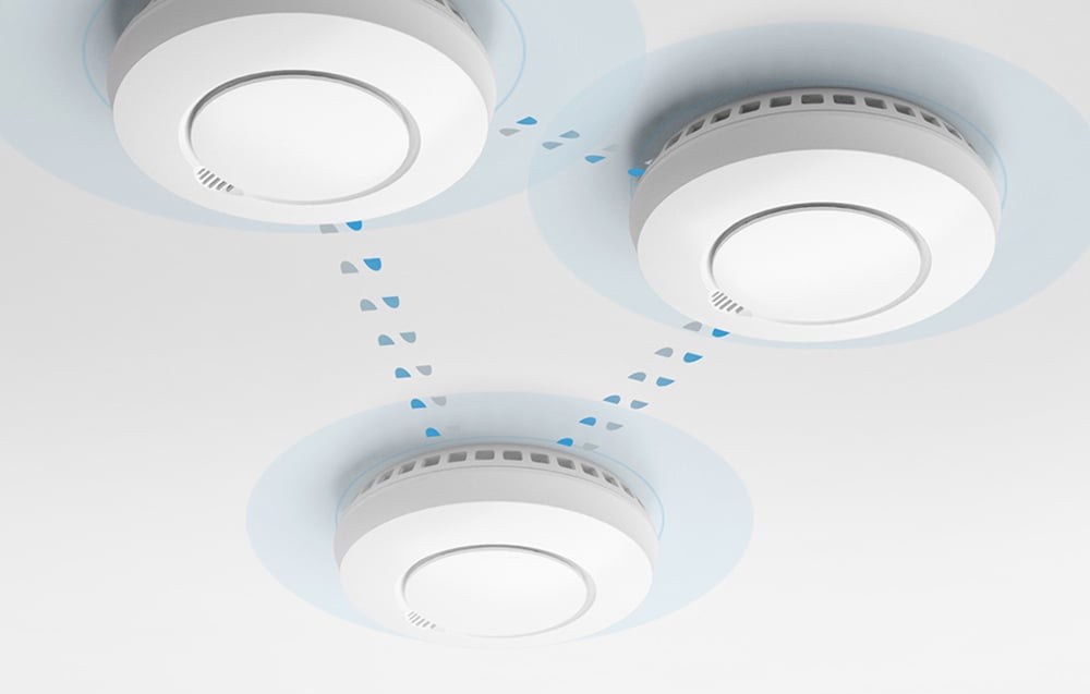 Three white smoke detectors on the ceiling communicating with each other via droplets and blue mist