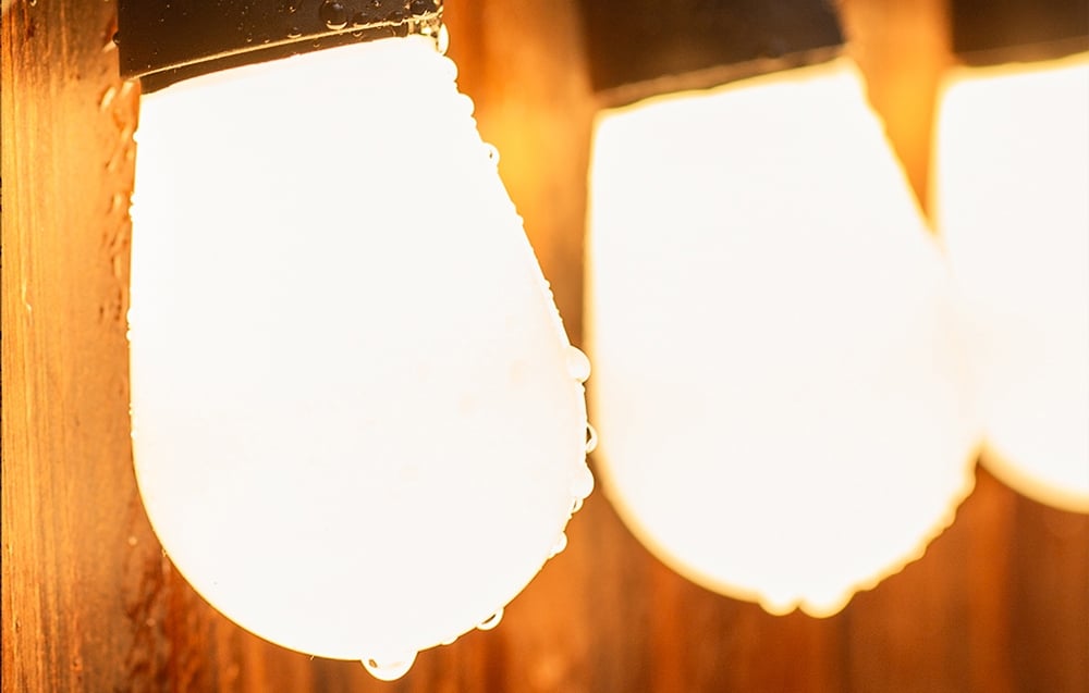A close-up of three string lights glowing with warm yellow light, with water droplets visible on their surface.