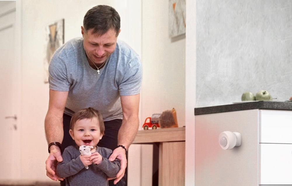 White motion sensor mounted on a kitchen cabinet in the background of a father with a child playing at home