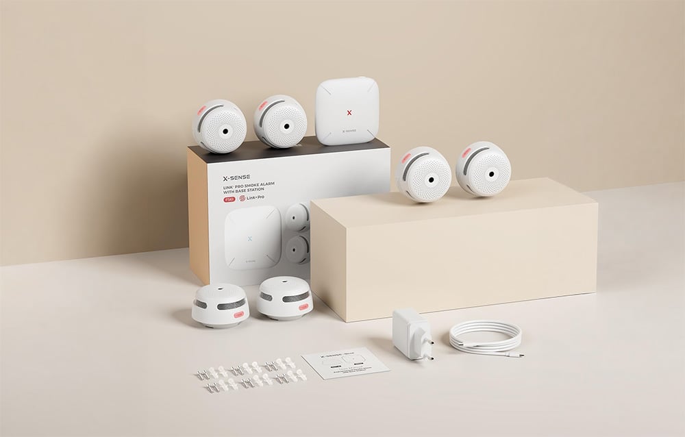 X-Sense kit: six smoke detectors, base station, box, power adapter, cable, and mounting hardware on a light background