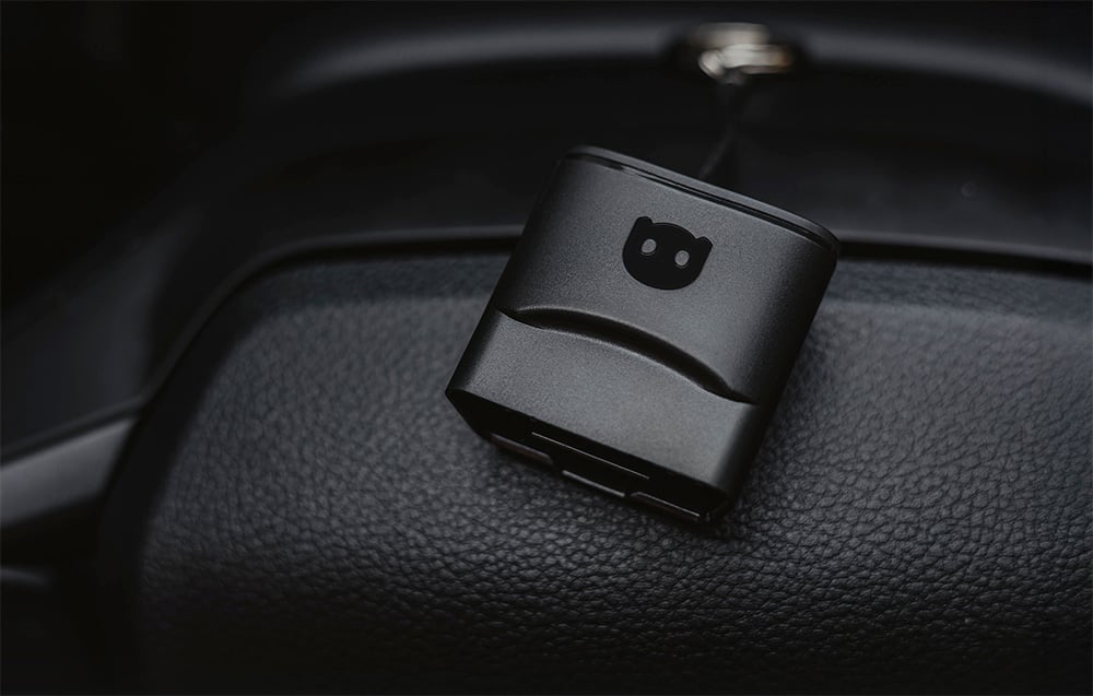Black Carly OBD2 diagnostic adapter lying on the car's leather dashboard