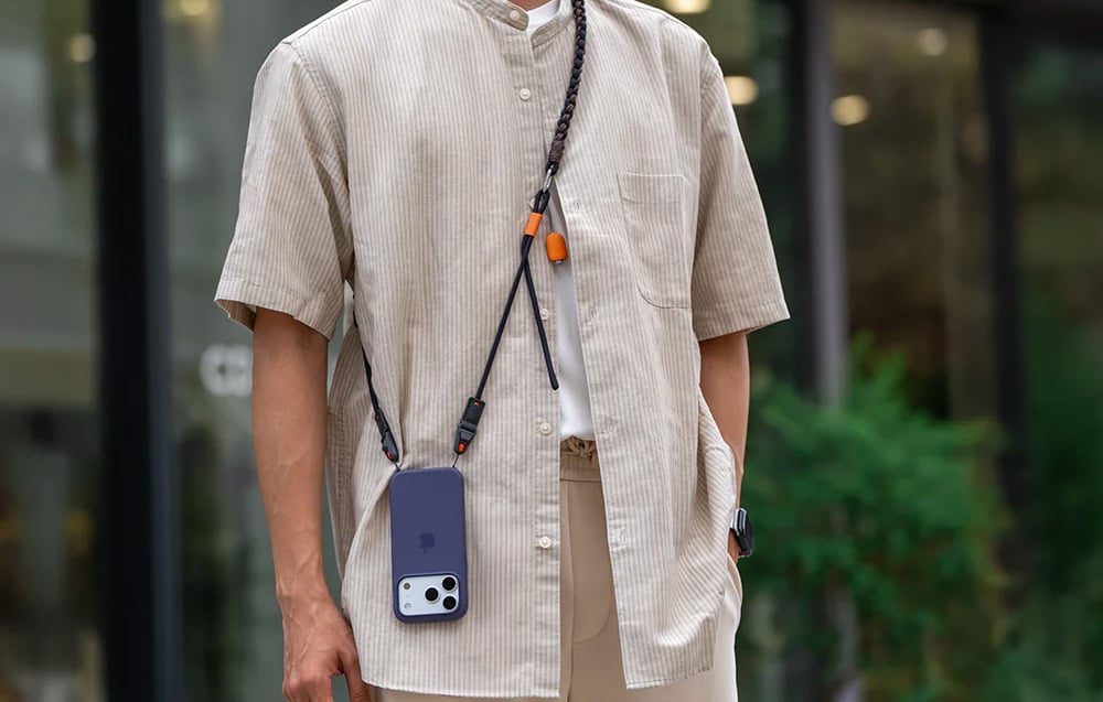 Man in cream shirt wears black neck strap, to which smartphone is mounted