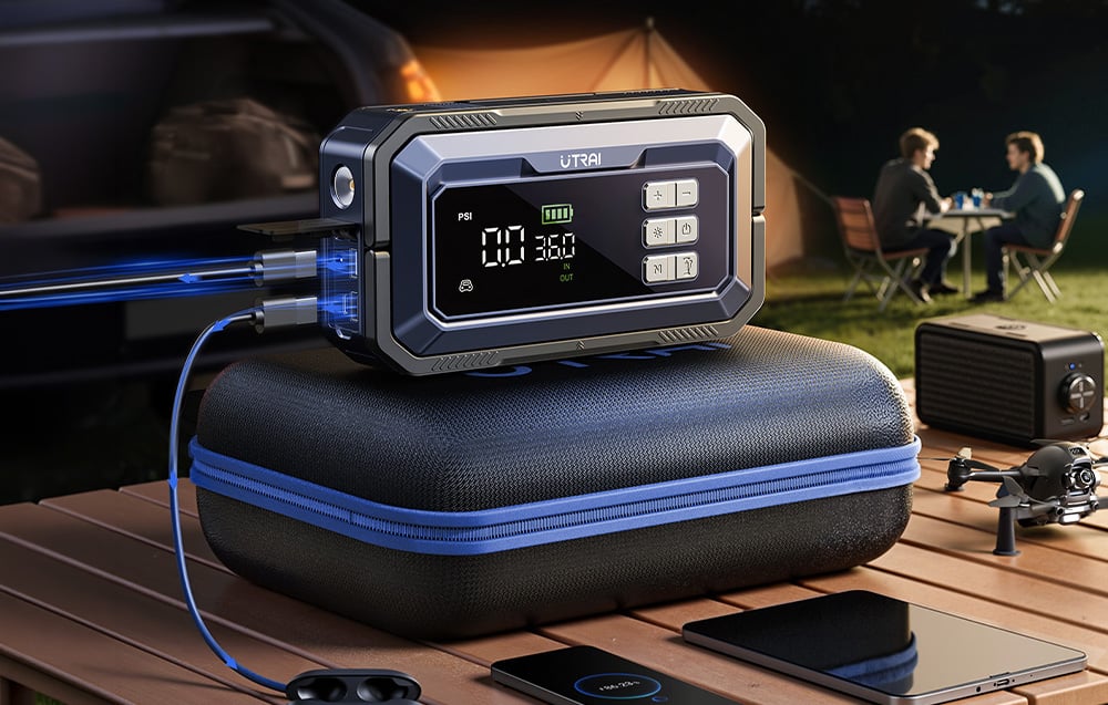 A car starter on a suitcase is charging a phone against a backdrop of a tent and people talking.