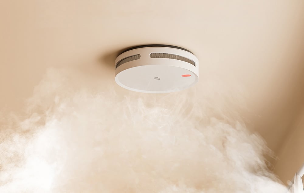 Smart smoke detector on the ceiling, with light-colored smoke rising below