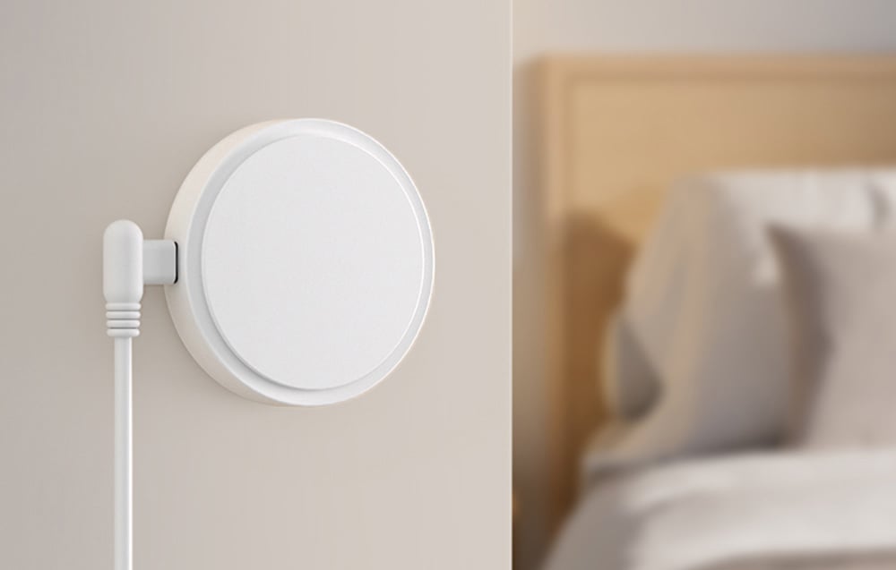 Round white sensor with wire mounted on the wall next to the bed in the bedroom