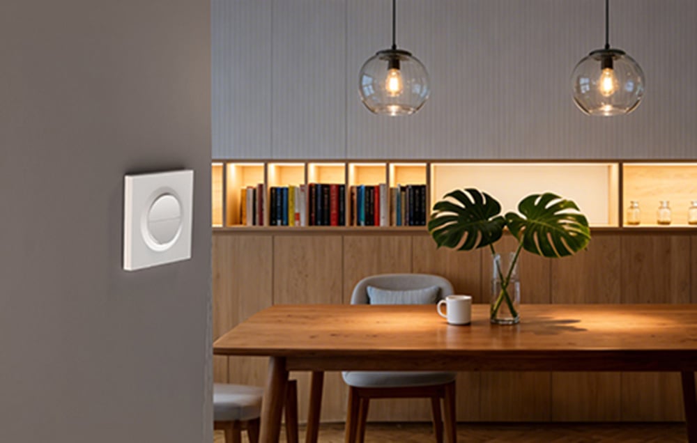 Elegant white SONOFF wall switch in modern dining room with wooden table, pendant lighting and illuminated bookcase