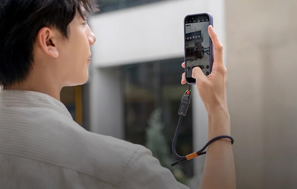 A man photographs a building with his smartphone mounted to a PGYTECH strap