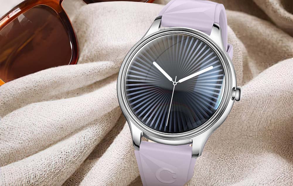 A silver smartwatch with a purple geometric strap and a dark striped dial, lying on a light-colored fabric next to sunglasses.