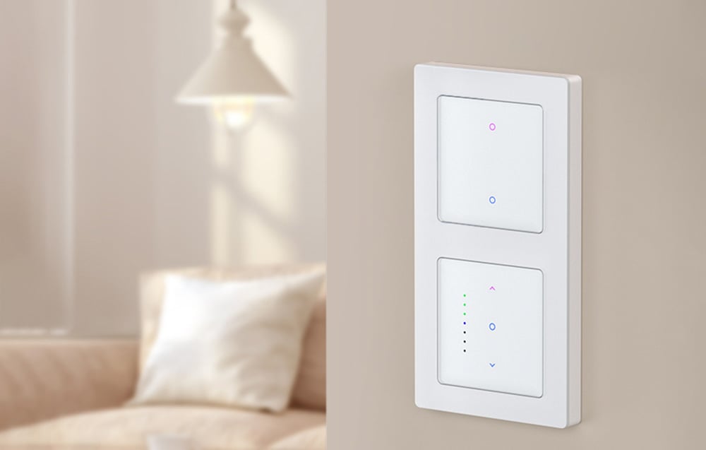 2 touch light switches on bright wall, couch with cushion and lamp in background