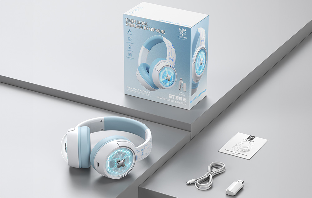 Gaming headphones lying on a gray table next to a box, user manual, USB adapter, and cable