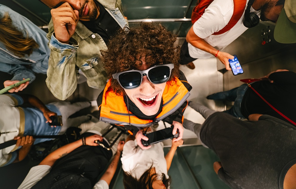 A person in an orange vest laughs while wearing XR glasses surrounded by other people