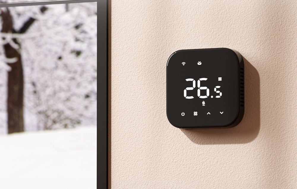 MEROSS smart thermostat on a light-colored wall next to a window with a winter landscape visible outside