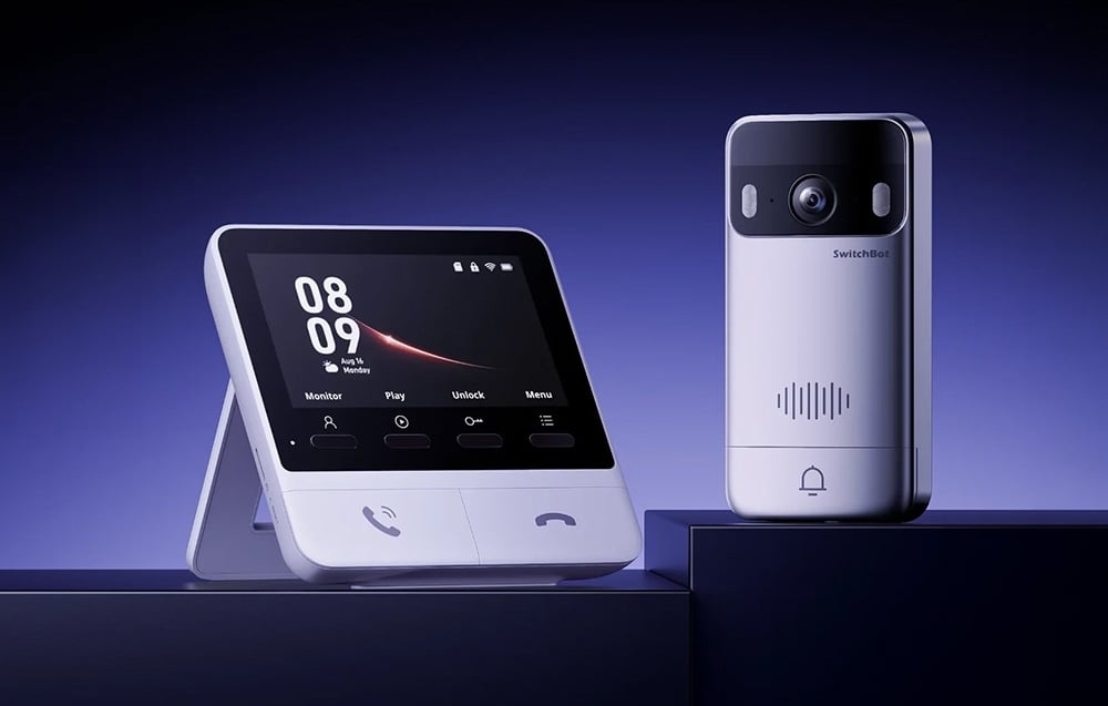 Silver outdoor doorbell with camera and white monitoring station with a screen on a dark purple background.