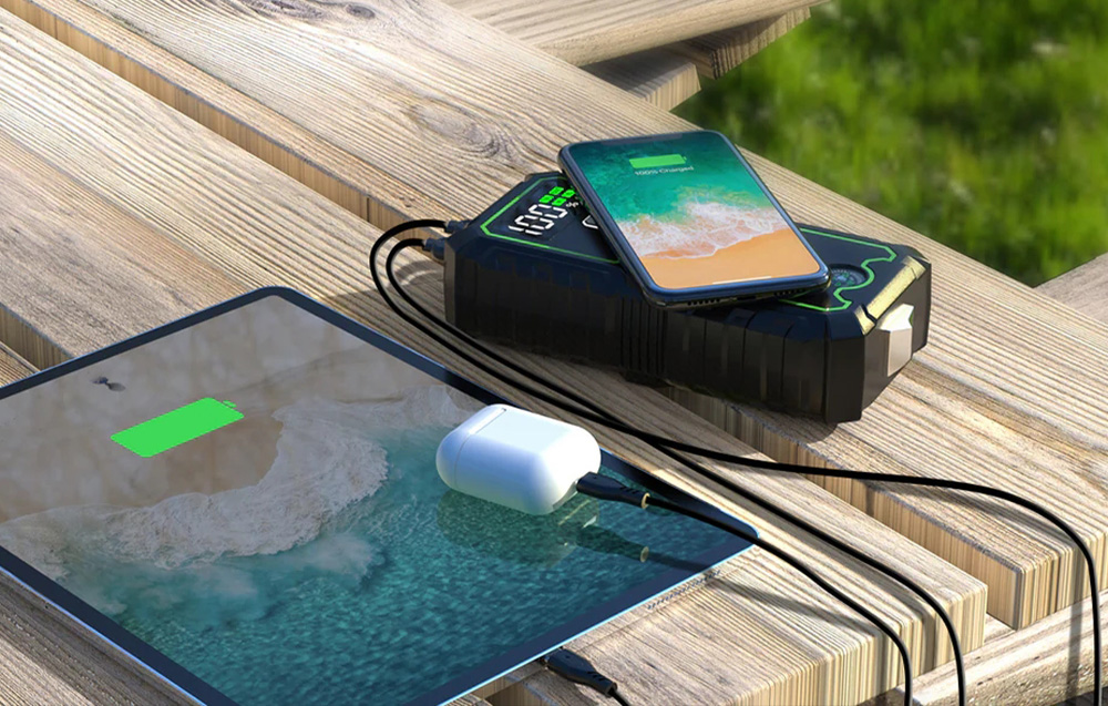 A large power bank simultaneously charging a phone wirelessly and a tablet via a cable.