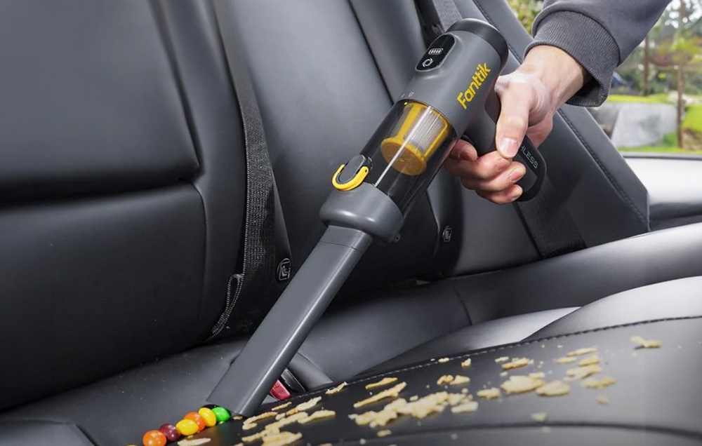 Portable vacuum cleaner with a narrow nozzle picks up dirt from the car's leather couch.